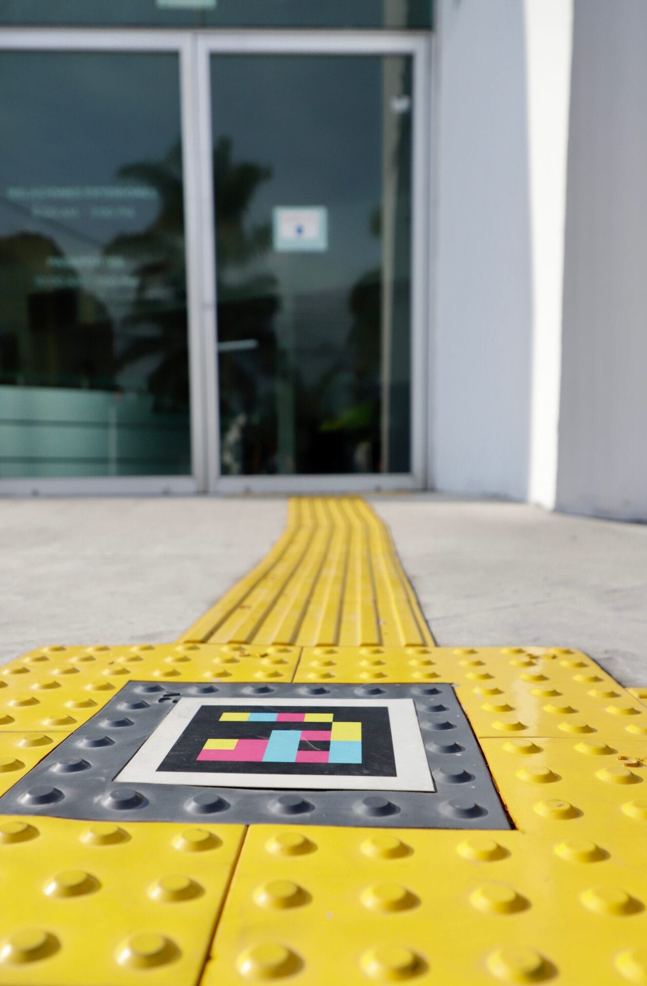 NaviLens code embedded in the yellow tactile paving right in front of the glass door of the Zapopan Foreign Affairs Passport Office, with a continuous guiding strip towards the entrance