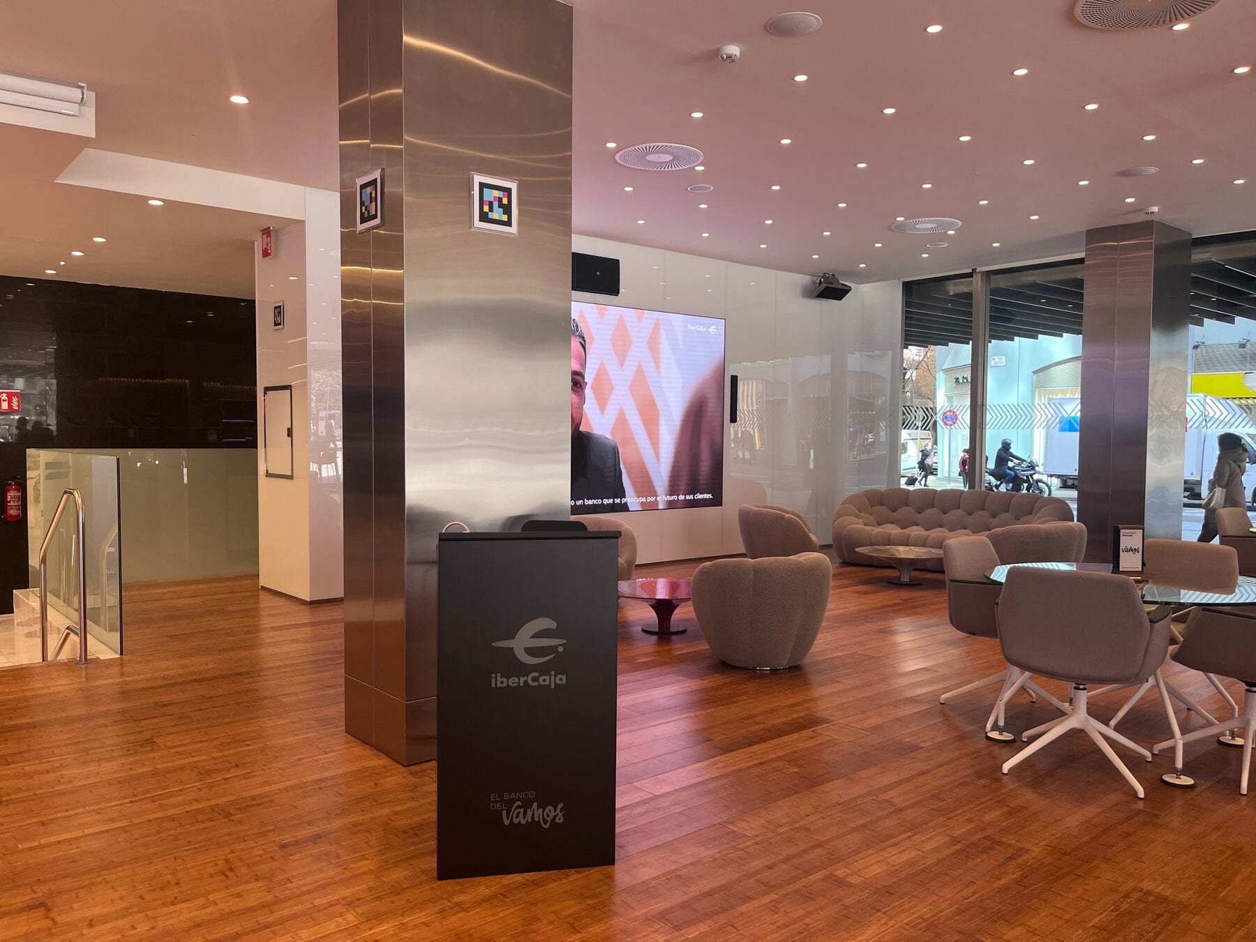 Zona de encuentro del Espacio Xplora con códigos NaviLens en las columnas cromadas y la gran pantalla corporativa de Ibercaja al fondo