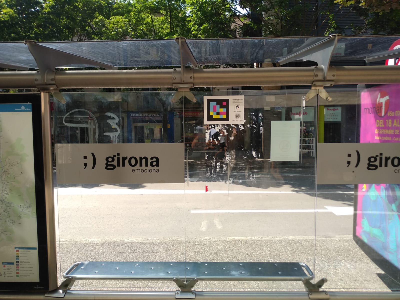 Girona bus shelter on Carrer de Santa Eugènia · Carrer Illa with the “;) girona emociona” sign, the City Council line map and a NaviLens code on the glass